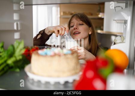 Junge Frau, die in der Küche eine Flasche Milch aus dem Kühlschrank nimmt Stockfoto