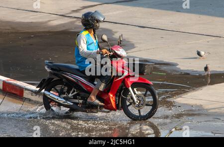 Der mototaxi-Fahrer in einer blauen Weste fährt auf der nassen Straße Stockfoto