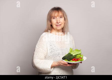 Glückliche ältere Frau Gemüse auf weißem Teller Porträt Stockfoto