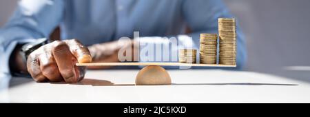 Geschäftsmann Balancing gestapelte Münzen mit Finger auf Holz- Wippe Stockfoto