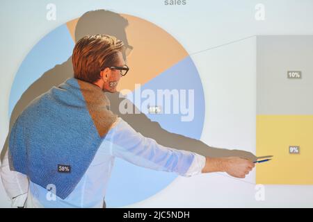 Rückansicht eines Geschäftsmannes in einer Brille, der vor der Projektionsleinwand steht und bei der Besprechung statistische Daten erklärt Stockfoto