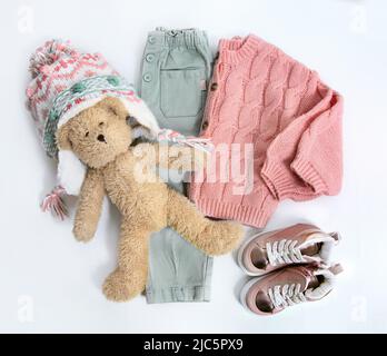 Winterkleidung für Kinder. Strickpullover, Hose, Hut und Spielzeug Draufsicht auf weißem Hintergrund. Mode Kinder warme Kleidung flach legen. Herbst Baby-Outll Stockfoto