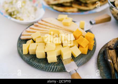 Blick auf Käse, Messer und Salatschüsseln auf dem Tisch. Käseplatte mit verschiedenen Käsesorten. Stockfoto