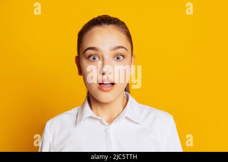 Schöne überrascht Mädchen mit langen lockeren Haaren Blick auf die Kamera mit breiten Augen isoliert auf gelbem Hintergrund. Konzept von Schönheit, Kunst, Mode, Gesichtsbehandlung Stockfoto