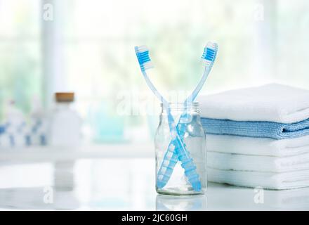 Zahnbürsten und Handtücher stapeln sich auf dem Tisch im Bad.Helcare und Hygiene.Zahnbürste im Glas. Stockfoto