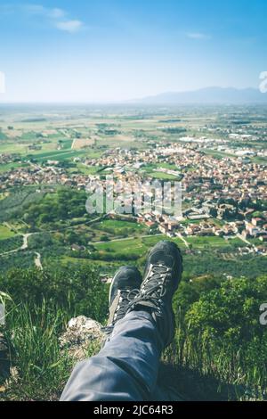 Trekkingschuhe und Bergpanorama. Männliche Beine und Füße mit technischen Wanderschuhen. Entspannen Sie sich auf der Spitze und genießen Sie die Landschaft. Freiheit, Outdoor-Lifestyle Stockfoto