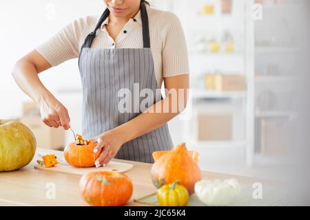 Nahaufnahme einer zufriedenen Frau in der Schürze, die an der Theke in der Küche steht und Kürbiskerne ausschaufelt Stockfoto