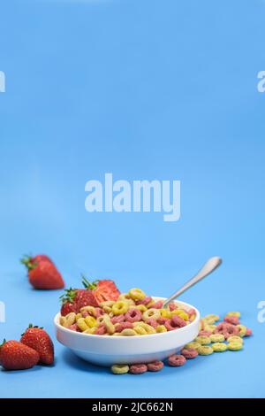 Maisringe mit Milch auf einem Teller mit Beeren und Früchten auf weißem Hintergrund. Das Konzept der schnellen Frühstückscerealien Stockfoto