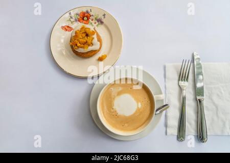 Blick von oben auf einen Latte und einen orangefarbenen Cupcake auf Vintage-Geschirr Stockfoto