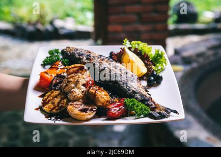 Das Fischgericht wird mit Gemüse, Kartoffeln und Gewürzen gegrillt. Stockfoto