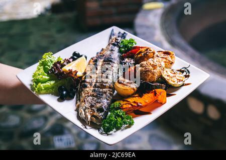 Das Fischgericht wird mit Gemüse, Kartoffeln und Gewürzen gegrillt. Stockfoto