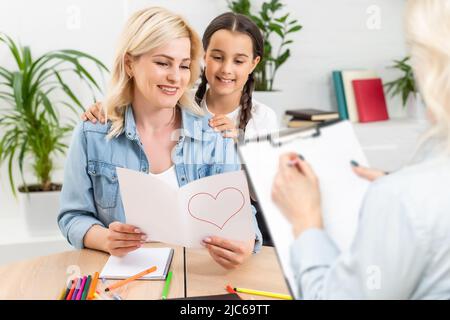 Hand eines professionellen Familien-Psychotherapeuten, der während einer Konsultation Notizen vor einer Familie mit einem Kind schreibt Stockfoto