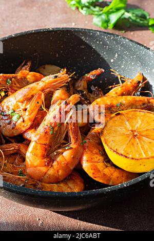 Gegrillte große Garnelen (Tiger) in einer Pfanne mit Gewürzen, Kräutern und Zitrone auf dunklem Grund gekocht. Stockfoto