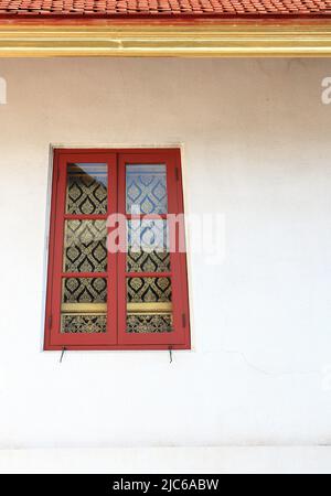 Staubige weiße Fassade eines alten Gebäudes mit einem kleinen schönen roten Holzfenster. Stockfoto