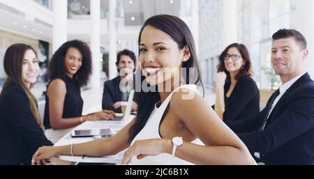 Ausgeschnittene Aufnahme einer jungen Geschäftsfrau, die während eines Gesprächs mit ihren Kollegen im Hintergrund in einem Büro lächelt Stockfoto