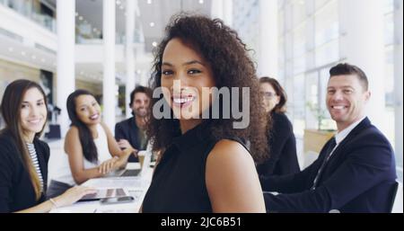 Ausgeschnittene Aufnahme einer jungen Geschäftsfrau, die während eines Gesprächs mit ihren Kollegen im Hintergrund in einem Büro lächelt Stockfoto