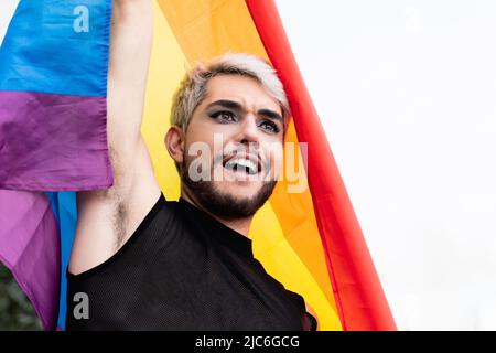 Gay Transgender Mann mit Make-up hält Regenbogen Flagge im Freien - LGBTQ Drag Queen Konzept Stockfoto