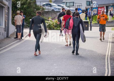 Surfer, die ihre Surfbretter tragen und eine Straße entlang im Stadtzentrum von Newquay in Cornwall gehen. Stockfoto