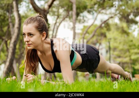 Schöne Brünette Frau trägt Sport-BH auf Stadtpark stehen, im Freien tun Plank-Übung auf Yoga-Matte und freuen uns. Gesunder Lebensstil, w Stockfoto