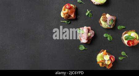 Dänische Snacks - Smorrebrod. Smorrebrod, traditionelle dänische offene Sanwiches von oben. Eine Reihe dänischer Sandwiches auf dunklem Hintergrund. Speicherplatz Kopieren. Stockfoto