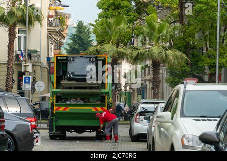 Batumi, Georgia - Mai 31 2022: Zwei Plünderer arbeiten zusammen, um Mülltonnen für die Müllentsorgung zu leeren, indem sie einen LKW zum Verladen von Abfällen benutzen. Konzept der Ökologie Stockfoto