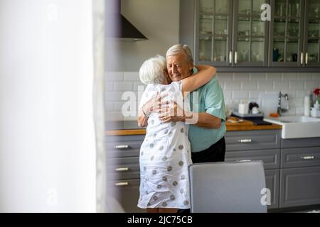 Das ältere Paar umarmt sich in ihrer Küche Stockfoto