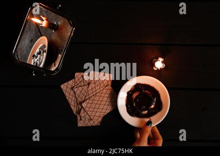 Eine brennende Kerze wurde von Spiegeln getragen und es gibt Wahrsagerkarten und Kaffeesatz auf einem Teller in der Nähe, Wahrsagerei auf Karten von Candleli Stockfoto