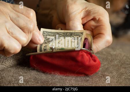 Die Hände einer alten Frau nehmen eine Dollarnote aus einer weichen roten Brieftasche, Geld in einer Brieftasche, Finanzen Stockfoto