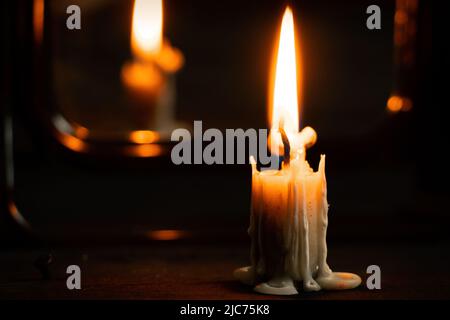 Brennende Kerze steht auf einem schwarzen Holztisch im Dunkeln in der Nähe des Spiegels, Kerzenfeuer im Dunkeln, Religion Stockfoto