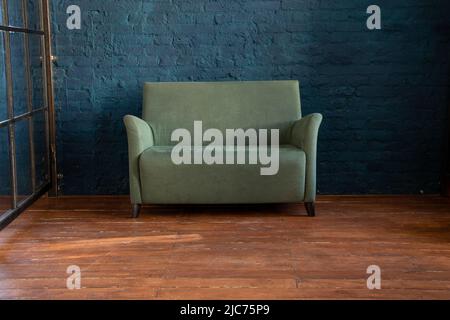 Grünes weiches Sofa in der Nähe der blauen Wand auf dem Holzboden im Zimmer, Polstermöbel in der Wohnung, Sofa im Flur, Minimalismus Stockfoto
