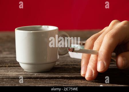 Eine Zigarette in den Händen eines Mädchens auf dem Tisch neben einer Tasse Kaffee, Zigaretten und Kaffee, schlechte Gewohnheiten, Rauchen Stockfoto