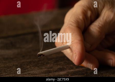 Frau, die eine Zigarette zu Hause am Tisch hält, im Dunkeln zu Hause raucht, Nikotin und schlechte Angewohnheit, Zigaretten und Krebs und Rauchen Stockfoto