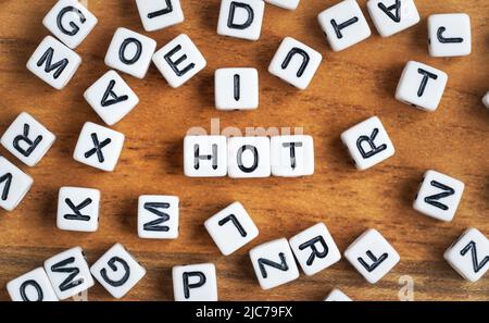 Kleine weiße und schwarze Perlenwürfel auf Holzbrett, Buchstaben in der Mitte zaubern HEISS Stockfoto