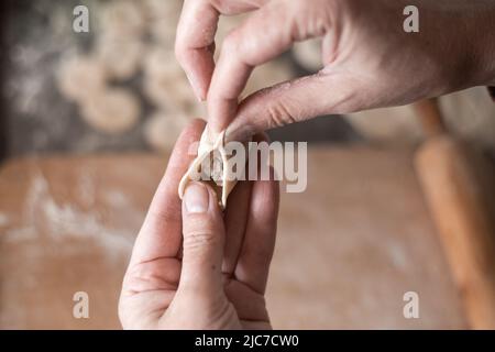 Eine Frau in der Küche formt Knödel aus Teig mit Fleischfüllung. Kochen köstliche hausgemachte Knödel. Stockfoto