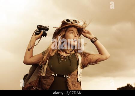Ein fröhliches junges Teenager-Mädchen verkleidet sich als Entdecker. Sie trägt einen Safarihut und hält ein Fernglas in der Hand. Stockfoto