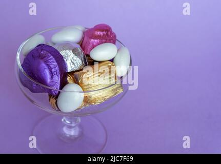 Festmahl-Konzept, traditionelle türkische Süßigkeiten aus dem Ramadan mit süßem Zucker und Pralinen auf Glas-Schale mit purpurfarbenem Hintergrund. Elegant. Stockfoto