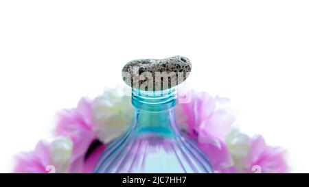 Transparente und türkisblaue Flasche mit einem Stein als Verschluss, umgeben von rosa und weißen Pastellfarben, die Schönheit und persönliche Betreuung darstellen Stockfoto