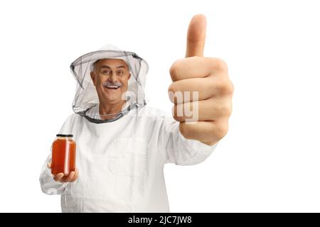 Bienenhalter in einer Uniform, hält ein Honigglas und stigt die Daumen isoliert auf weißem Hintergrund hoch Stockfoto