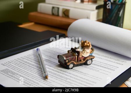 Bild eines Kinderwagens auf einem Kaufvertrag auf einem Tisch in einem Büro, mit verdeckten Büchern im Hintergrund Stockfoto