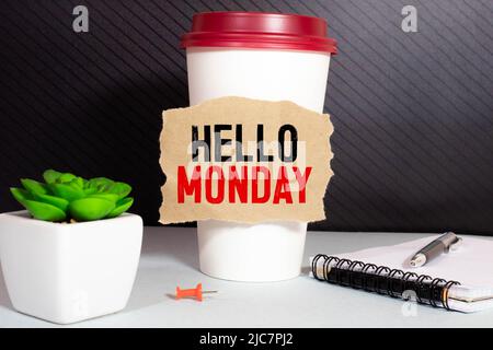 Draufsicht auf eine Tasse Kaffee, einen Stift, eine Sonnenbrille und ein Notizbuch mit „HALLO MONTAG“ auf weißem Holzhintergrund. Stockfoto