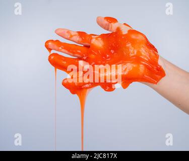 Roter Schleim, der aus der Hand einer Frau auf einem weißen Hintergrund herabfließt. Stockfoto