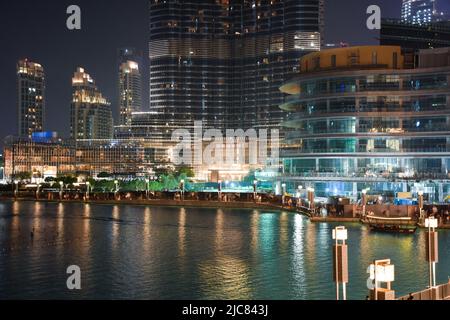 Beleuchtete Skyline der Innenstadt von Dubai mit dem Fuße des Burj Khalifa, der Uferpromenade und den Lichtreflexen der Stadt im Burj Lake. Stockfoto