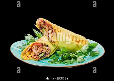 Hühnershawarma in Käsepita liegt auf einem Teller auf einem schwarzen isolierten Hintergrund Stockfoto