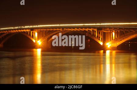 Hintergrundbeleuchtung auf einer Brücke über den Fluss, die sich nachts im Wasser spiegelt Stockfoto