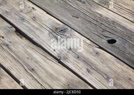 Holzboden aus alten Brettern mit Ästen und Rissen, verwittert durch Sand. Diagonale Ansicht Stockfoto