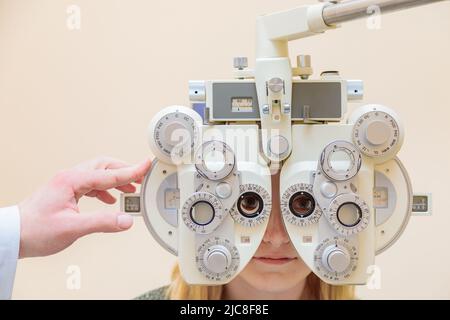 Ein männlicher Augenarzt überprüft das Augenlicht eines Mädchens mit einem Phoropter. Sehbehandlung. Stockfoto