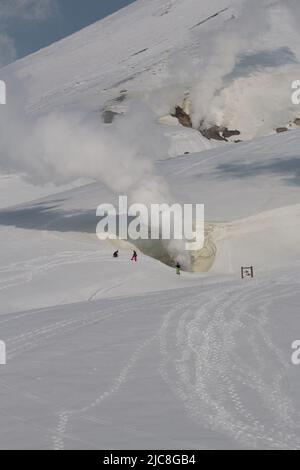 Touristen stehen in der Nähe von dampfenden vulkanischen Schloten in verschneiten Landschaften Stockfoto