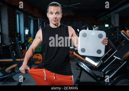 Junge attraktive Athlet männliche Gewicht mit Skala in der Turnhalle und Diät Stockfoto