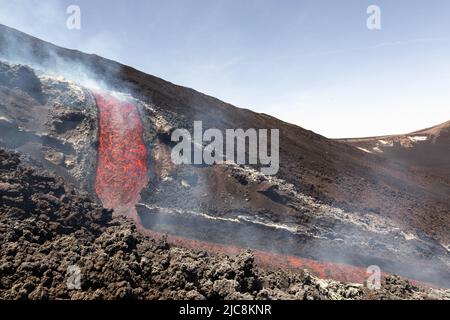 Etna Colata di Lava incandescente che scorre sul vulcano di Sicilia nella Valle del Bove con fumo e canale di scorrimento lavico Stockfoto