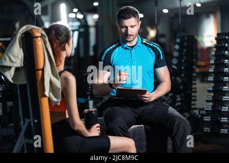 Junger persönlicher Trainer Mann im Gespräch mit Frau Athlet und planen Training im Fitnessstudio Stockfoto